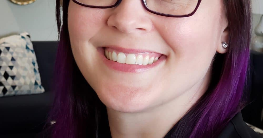 Headshot of Alicia Exsted, MA, LPCC, smiling, wearing dark-rimmed glasses and purple hair.