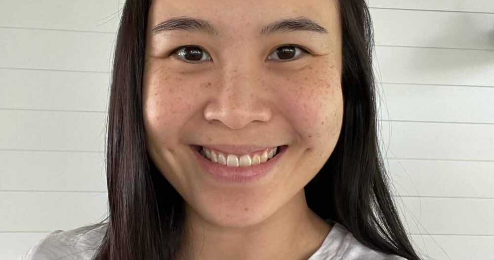 Headshot of a smiling woman with long black hair wearing a white top