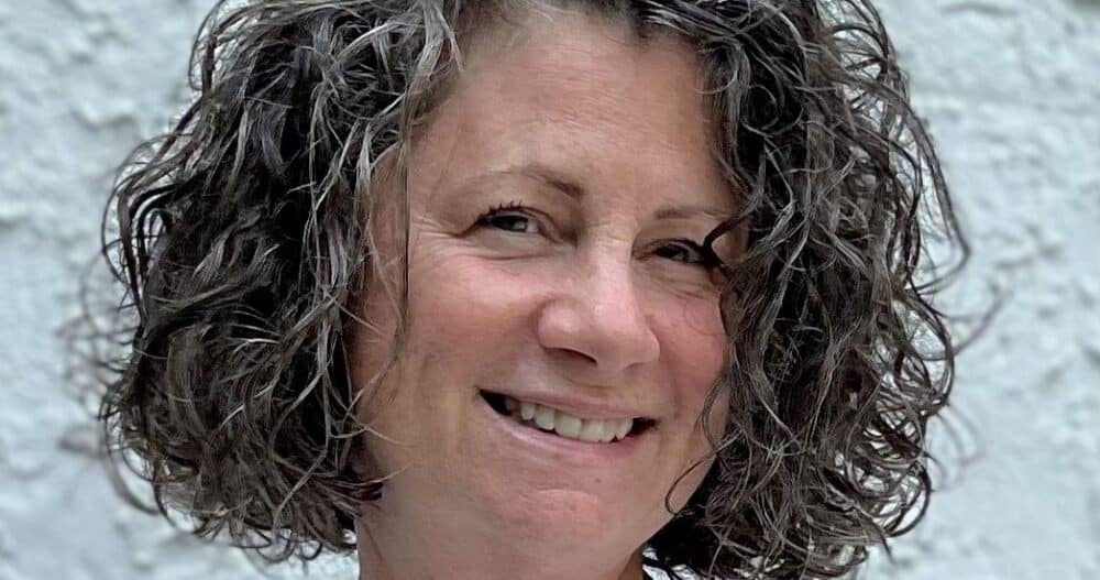 Headshot of a smiling woman with long, curly salt and pepper hair.