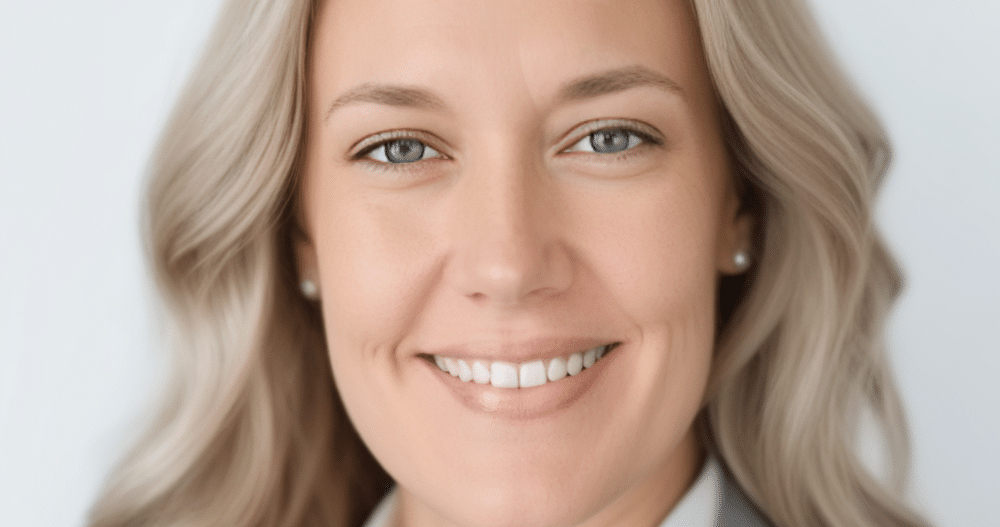 Headshot of a smiling woman with blond hair wearing a business suit and diamond earrings