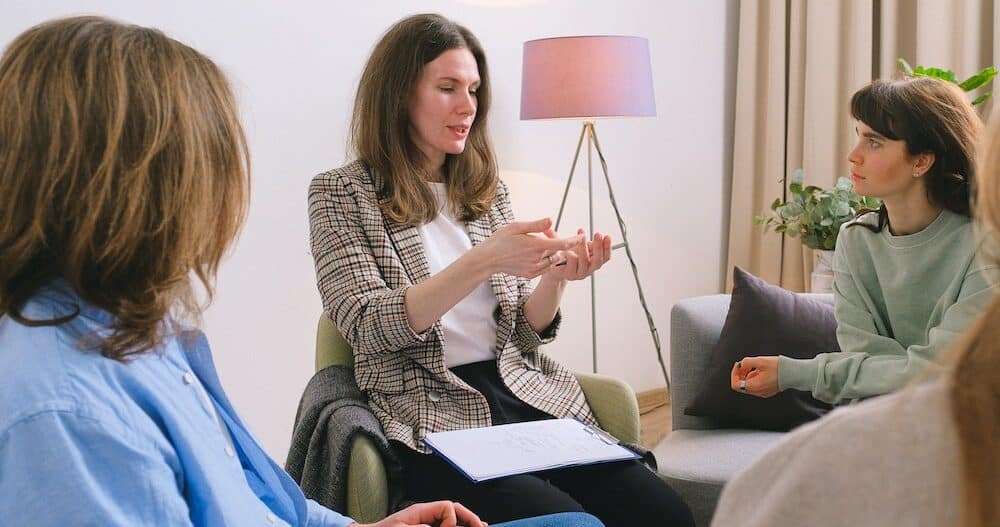 A group of women sitting with a therapist who is talking to them and taking notes