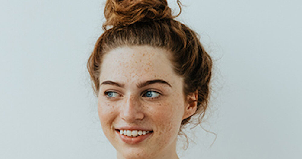 Girl with freckles is looking away and smiling, on a white background